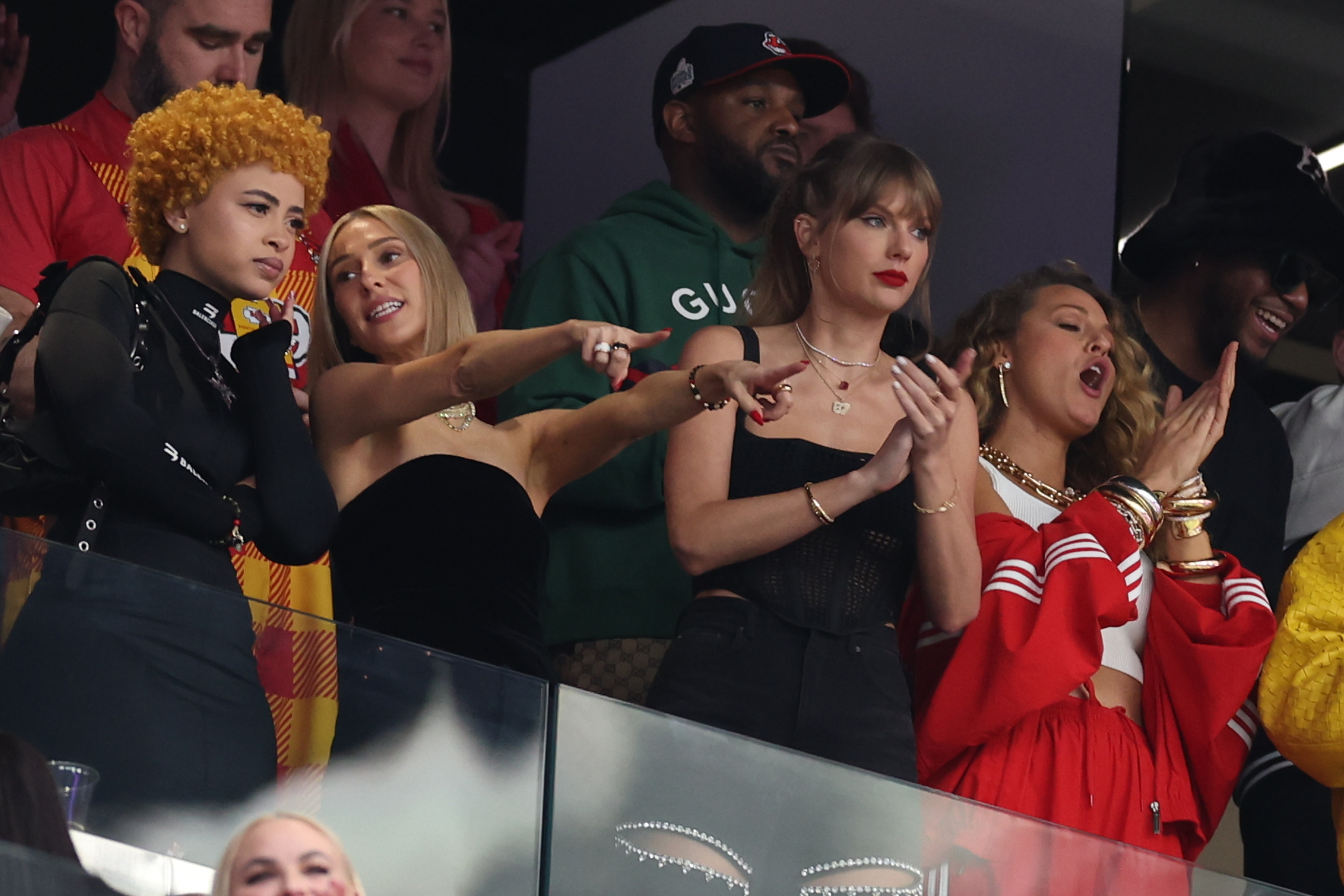 Group of people including Taylor Swift in a stadium box reacting excitedly during an event. Taylor is in a red outfit