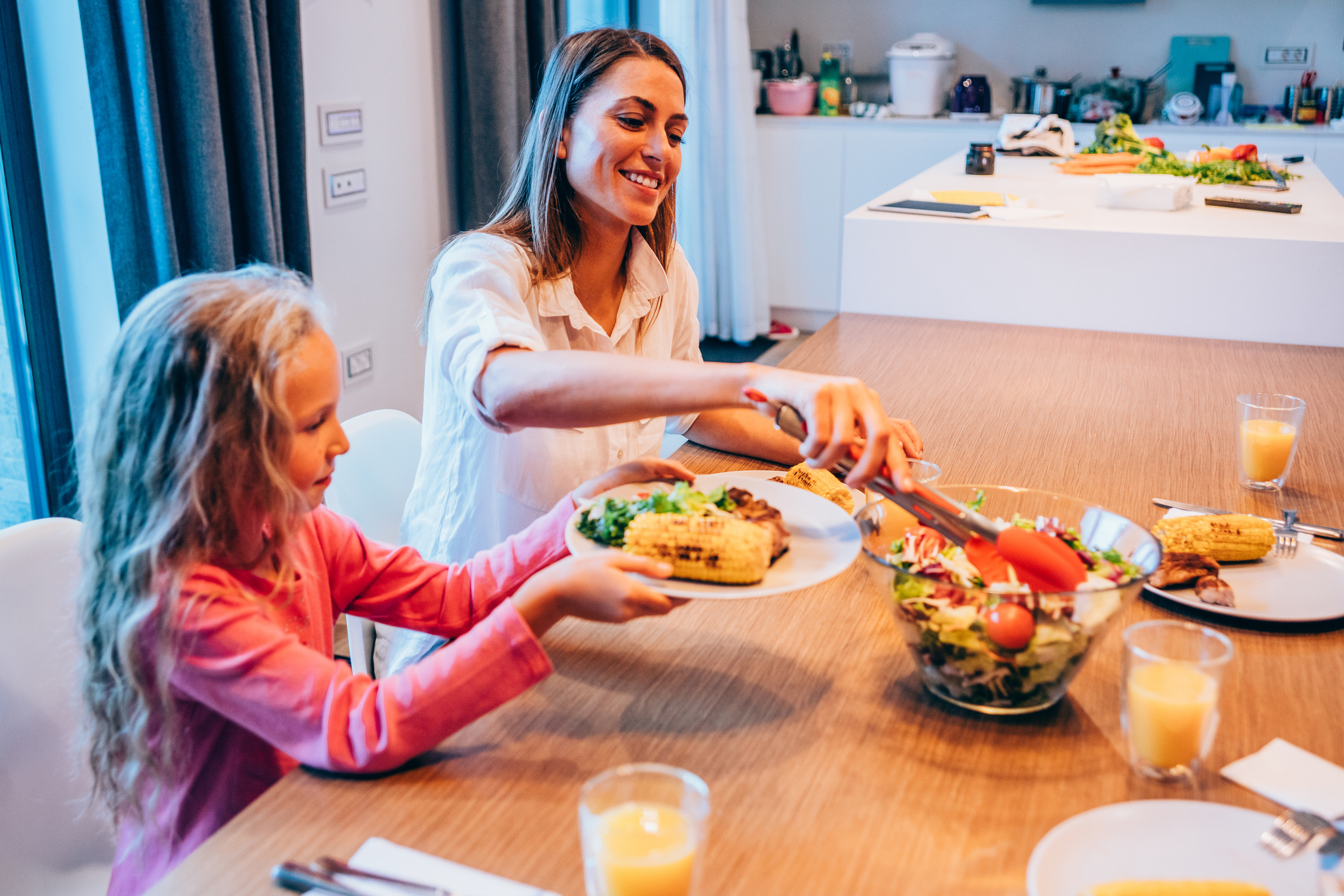 Mom and child enjoying a meal at a dining table, passing food, smiling together