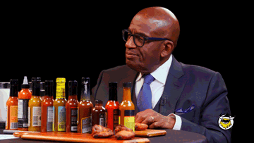 Al Roker reacts to tasting hot sauces on &quot;Hot Ones&quot; show, with lineup of sauce bottles on table