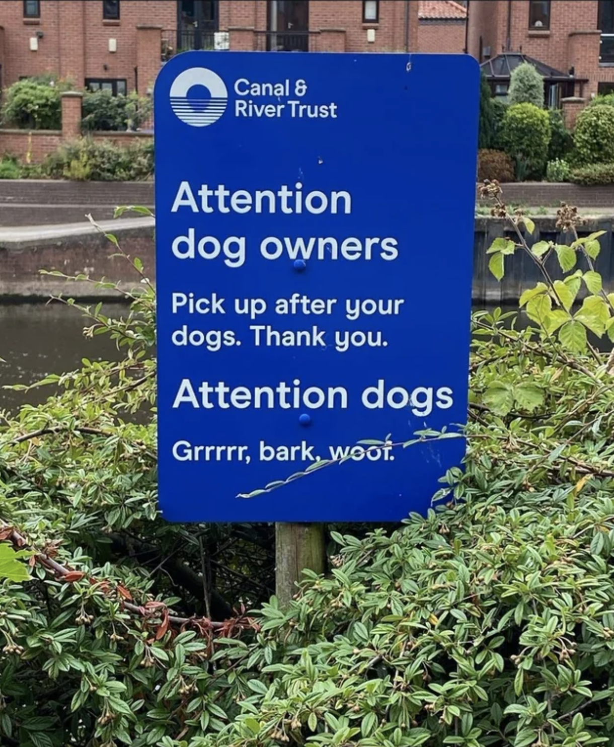 outdoor sign that tells owners to clean up after their dog and then addresses dogs with, grrr, bark, woof