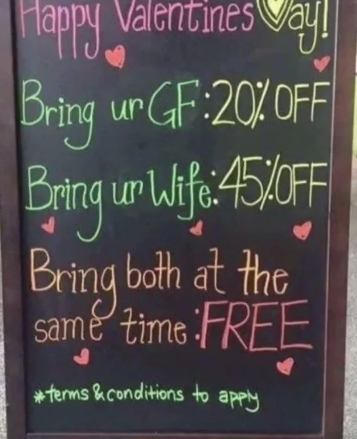 Blackboard with a Valentine&#x27;s Day offer, giving discounts based on relationship status, humorously suggesting a free offer for bringing both a girlfriend and wife. Terms and conditions apply