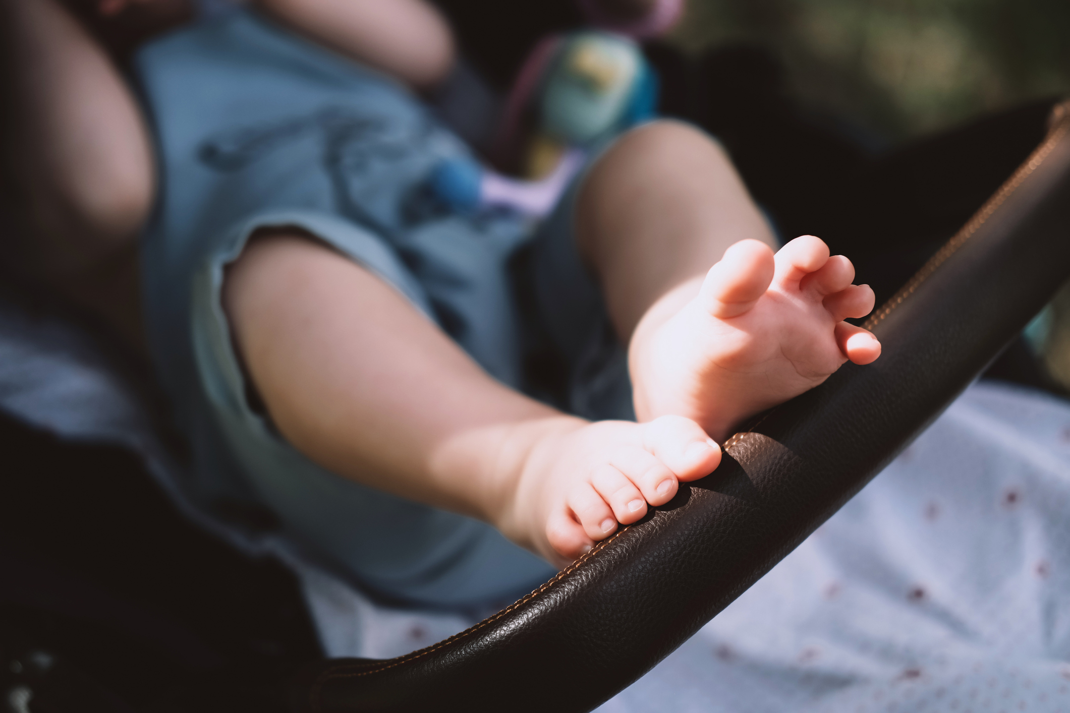 Toddler&#x27;s bare feet in a stroller, with a focus on safety harness