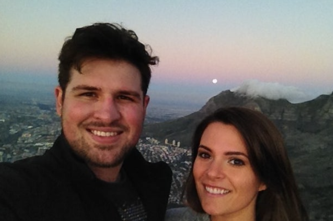 Two people taking a selfie with a scenic mountain and city view in the background