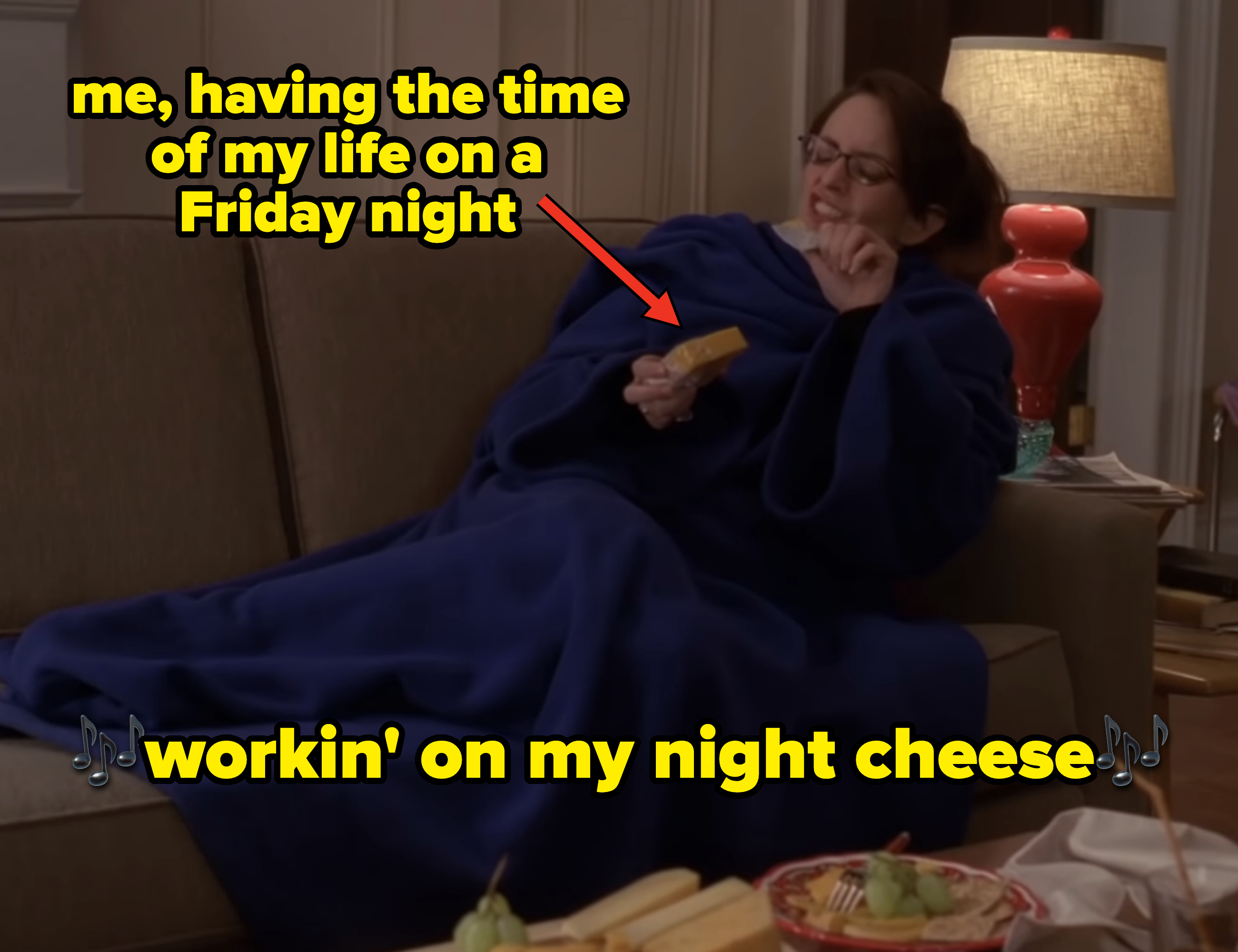 Woman wrapped in a blue blanket on a couch, laughing and holding a remote. Two plates of food on the coffee table