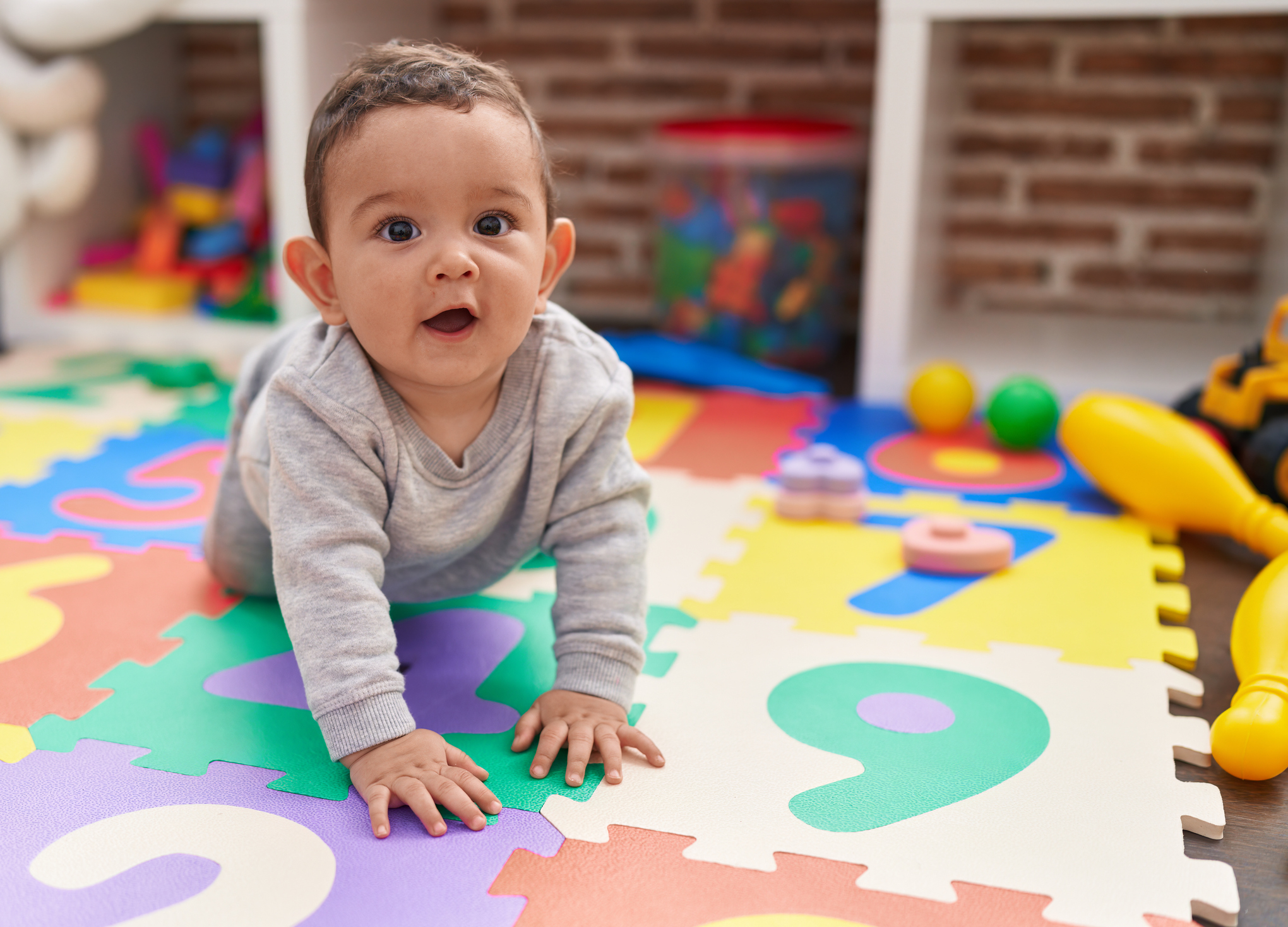 Baby crawling on an alphabet floor puzzle in a playroom