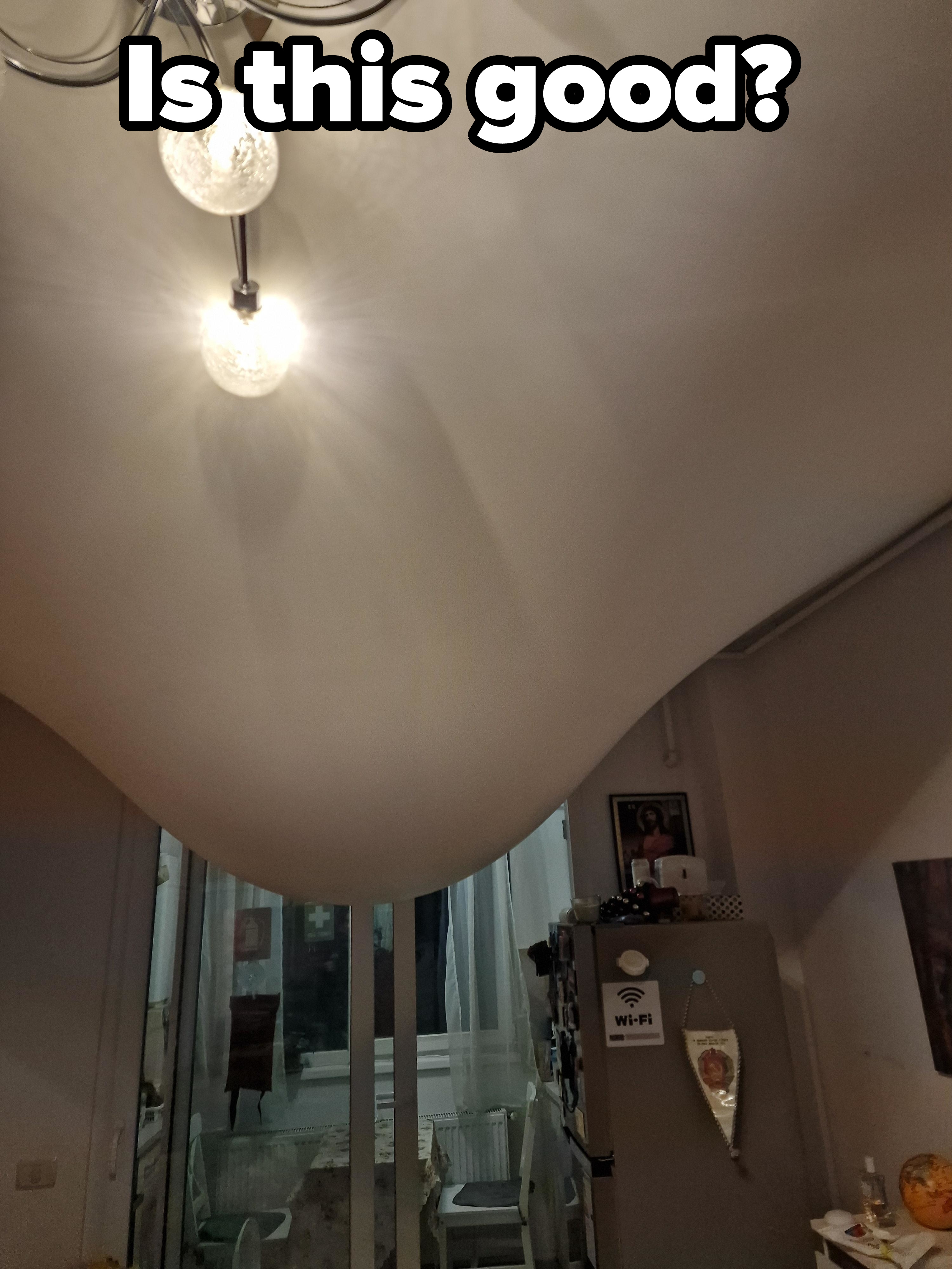 Ceiling light fixture on, illuminating a room with visible door at the end and a severely sagging ceiling