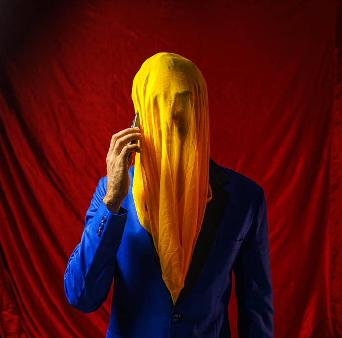Person in blue blazer with yellow fabric draped over head holding a mobile device to ear
