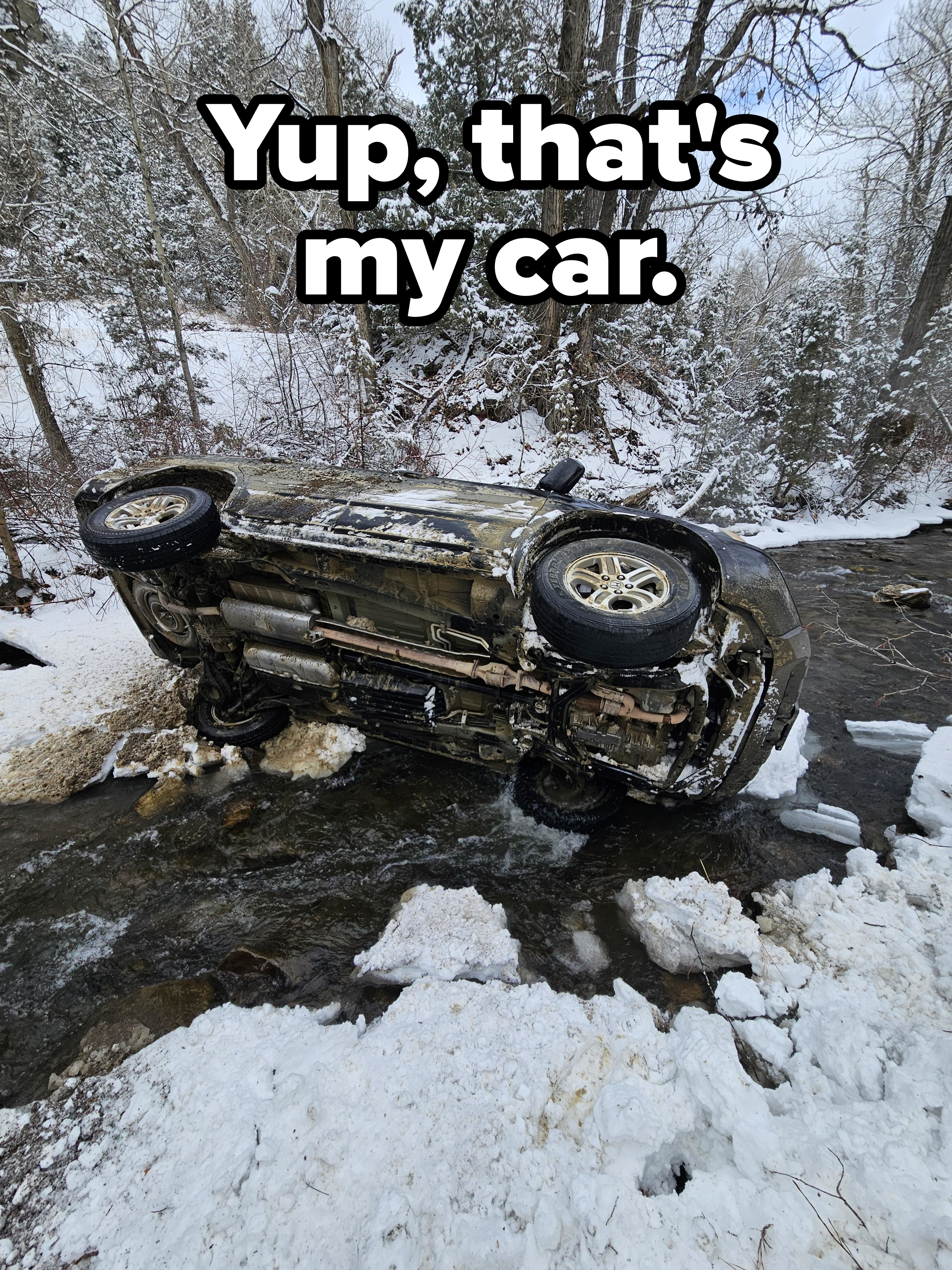 Overturned car in a snowy creek with trees in the background
