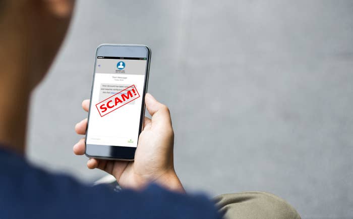 Person holding a smartphone with a warning screen alerting to a scam