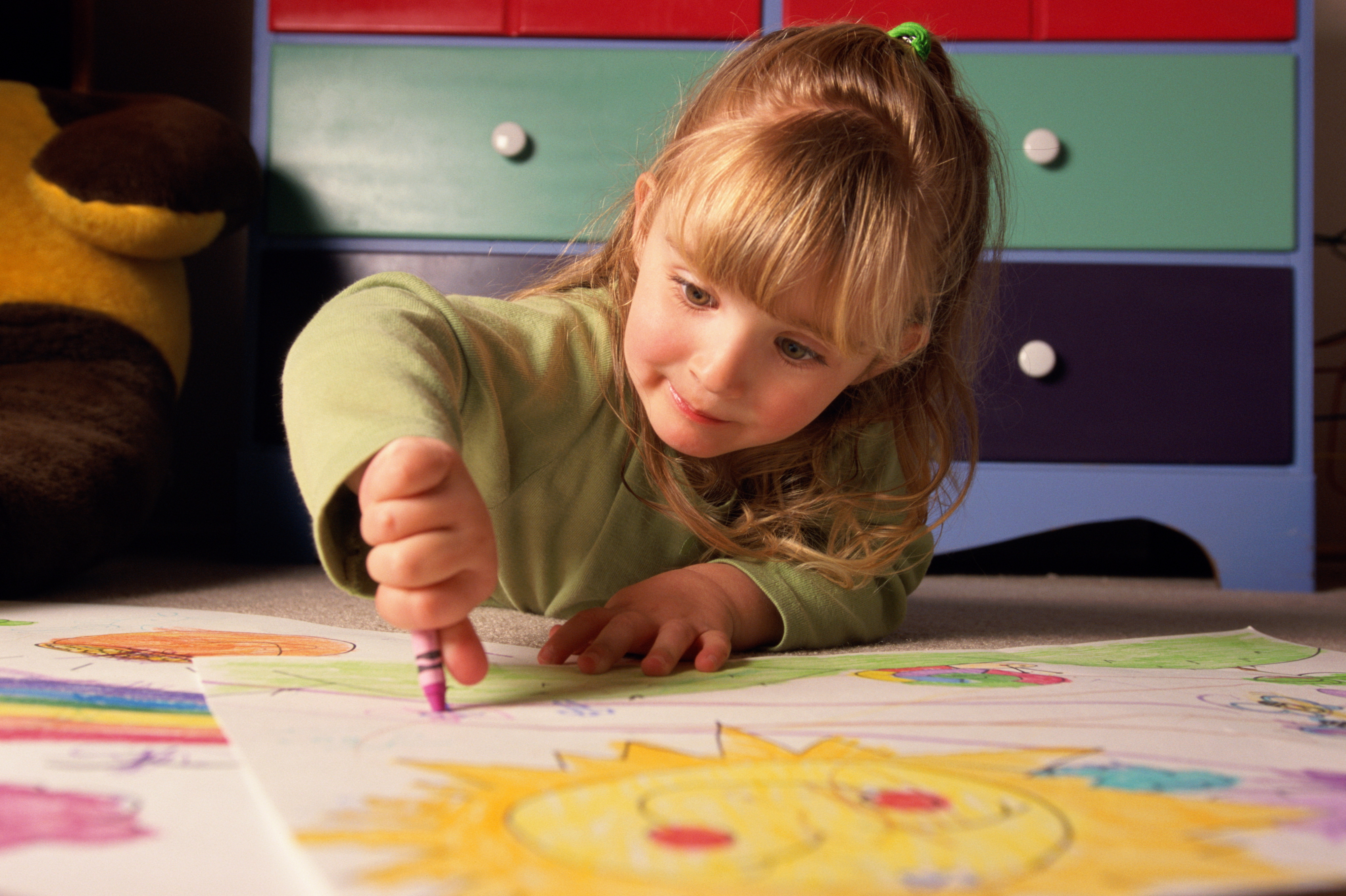 Child drawing on paper with crayons at a table, focused on artwork