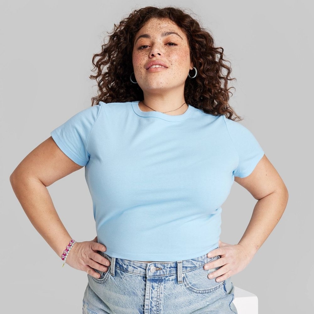 Confident woman in a blue t-shirt and jeans, hands on hips, look of determination