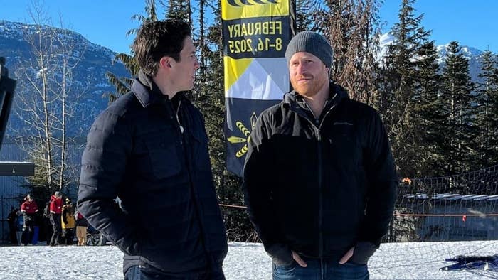 Prince Harry and a GMA anchor in winter jackets stand before a mountain landscape and a &quot;Freewheelers&quot; banner