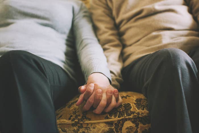 Two people seated closely, holding hands on a couch