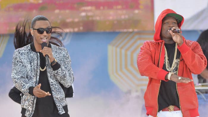 Two performers on stage, one in a patterned shirt and the other in a red hoodie, both wearing gold chains