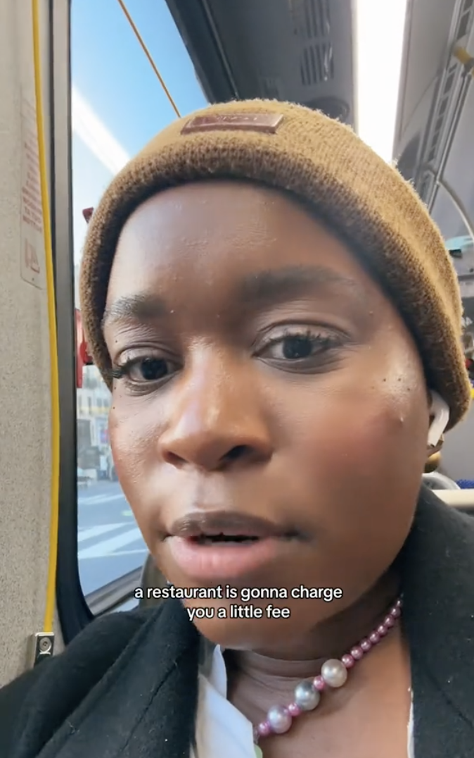 imani on a bus, looks at the camera with caption about restaurants charging fees