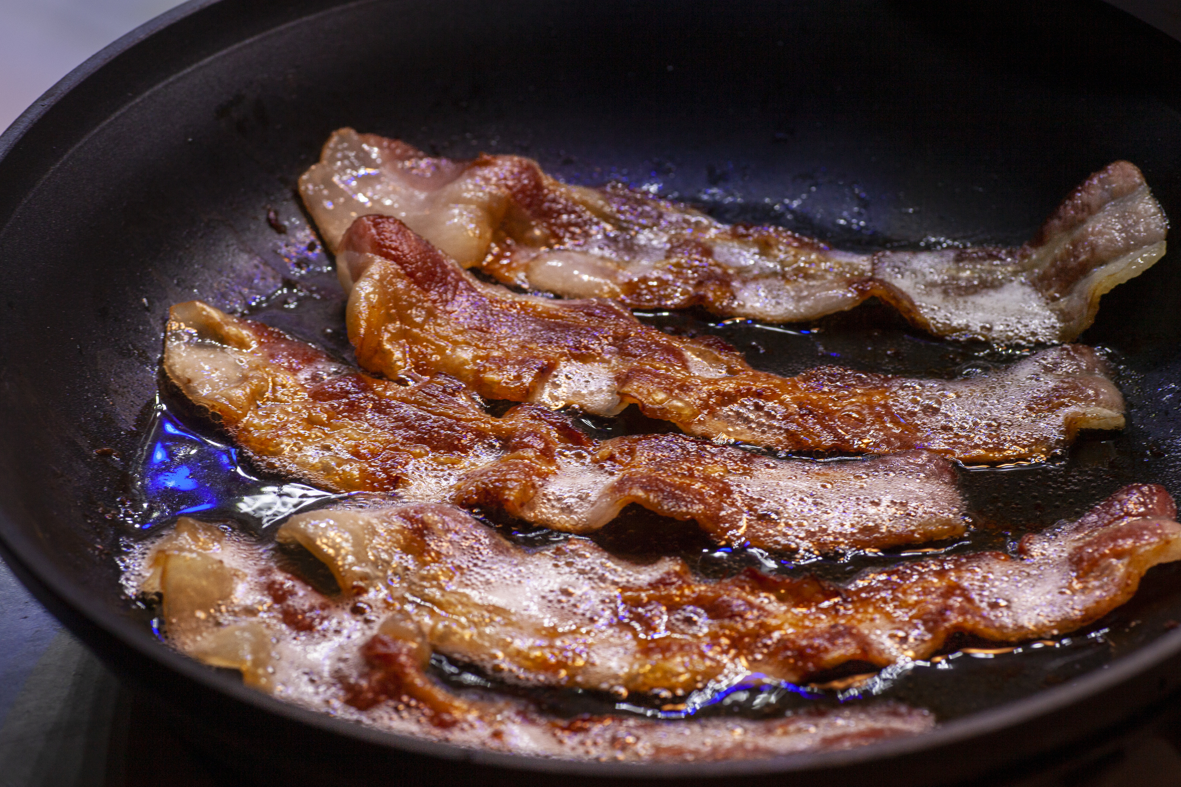 Sizzling bacon strips cooking in a skillet over a stovetop flame