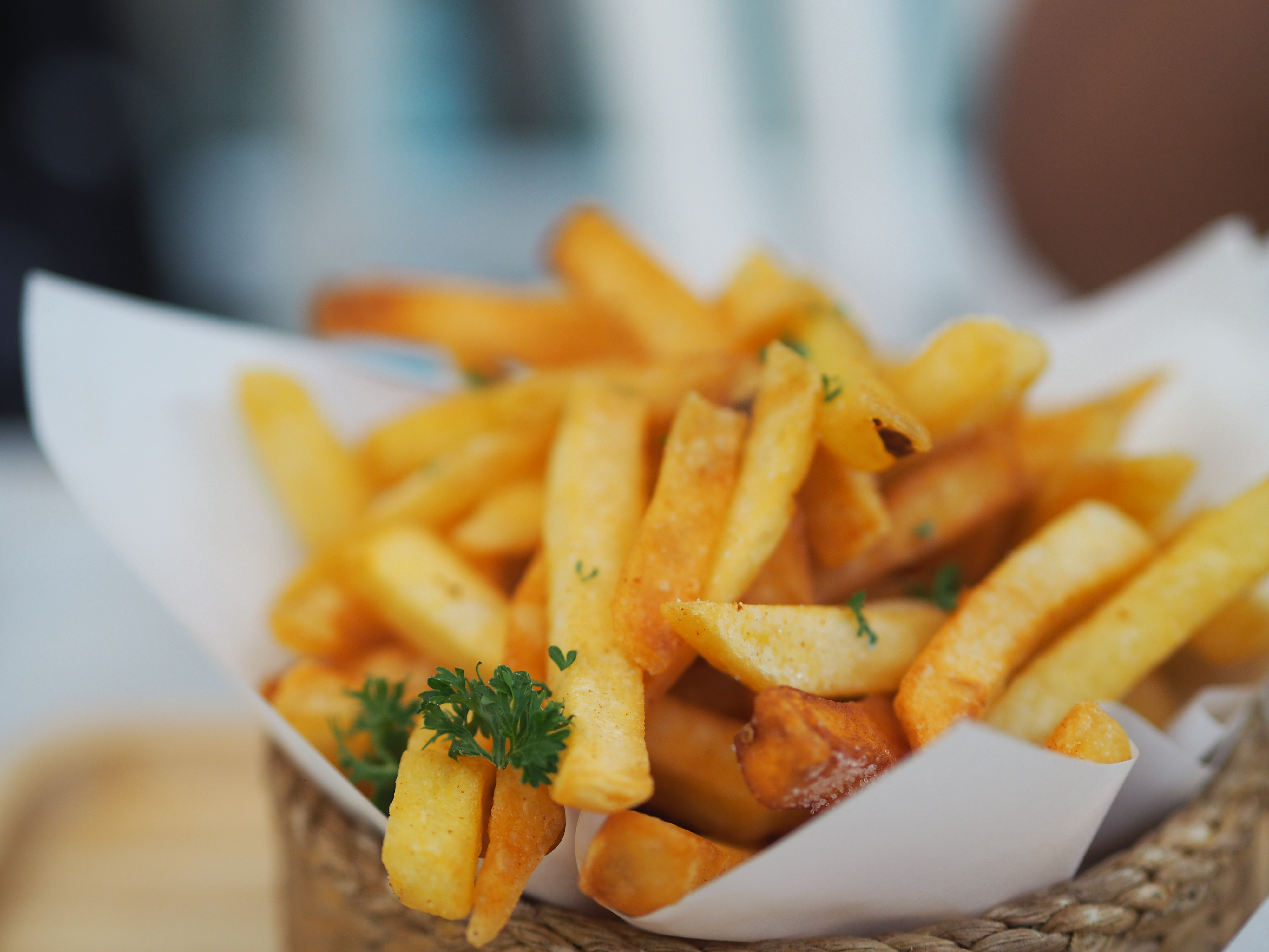 A close-up of freshly cooked French fries garnished with parsley in a paper cone