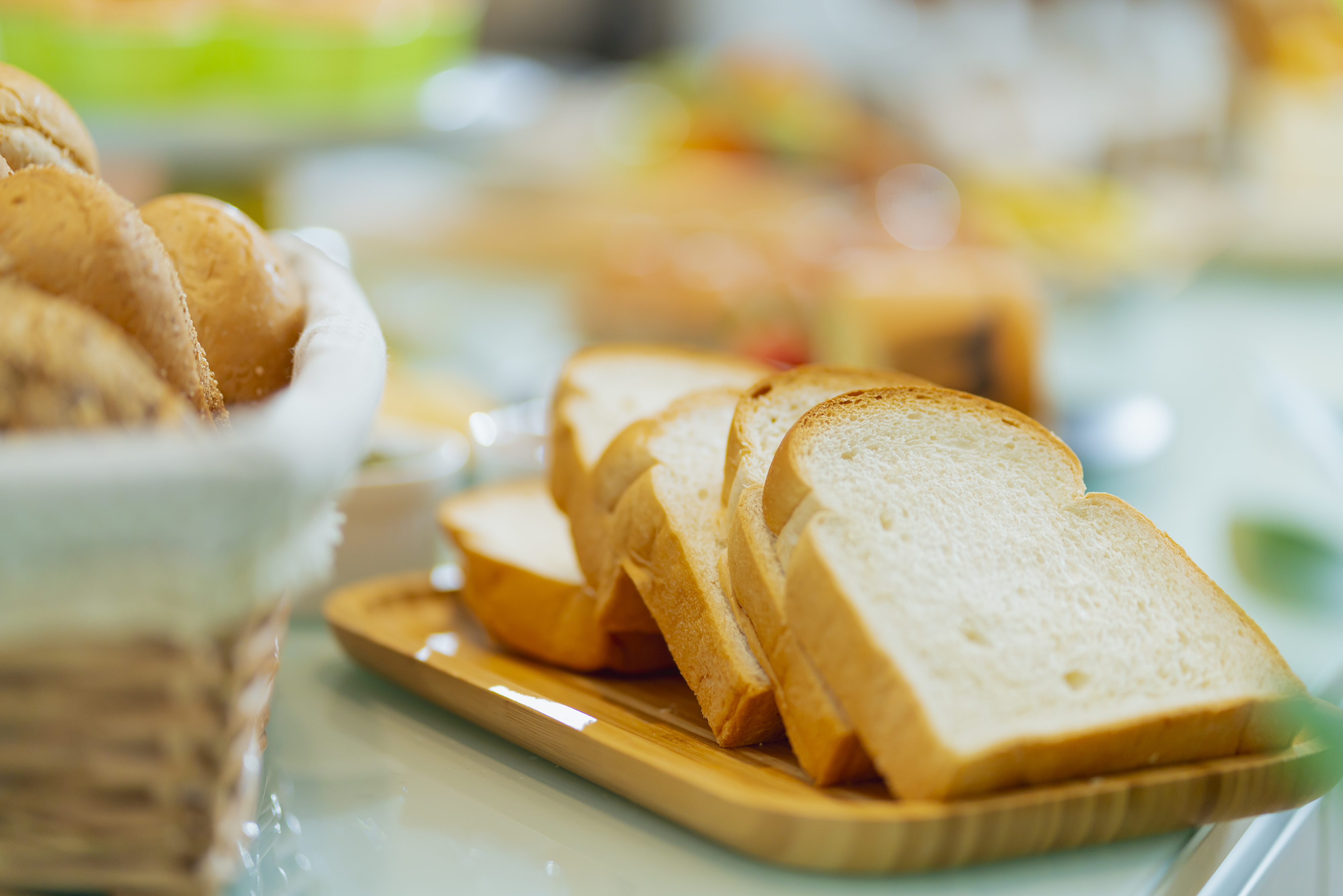 Sliced white bread on a plate, with additional food items blurred in the background
