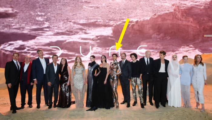 Group of people standing in front of a 'Dune' backdrop, some cast members in elegant evening wear