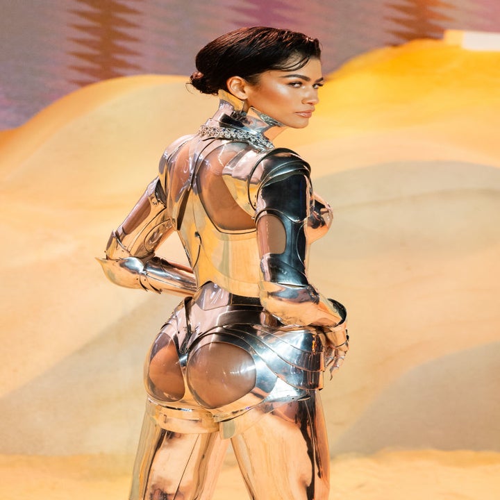 Woman in a metallic structured outfit looking over her shoulder on a desert-set backdrop
