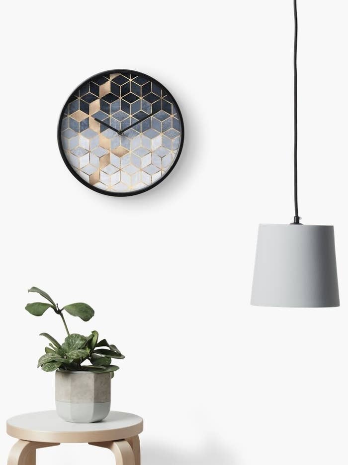Decorative wall mirror with geometric shapes above a plant on a small table, beside a hanging lamp