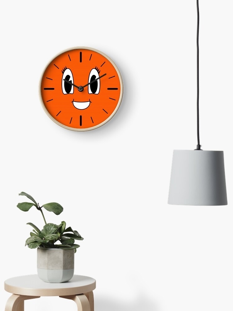 Wall clock with a cartoon face design above a plant on a table, next to a hanging lamp