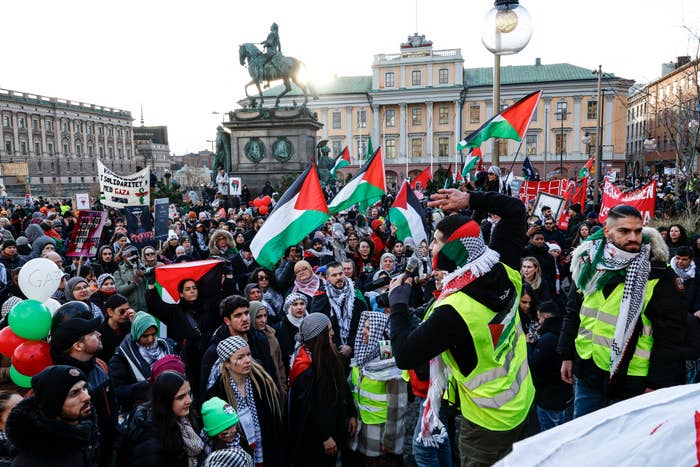Crowd at a rally with palestinian flags and a statue in the background
