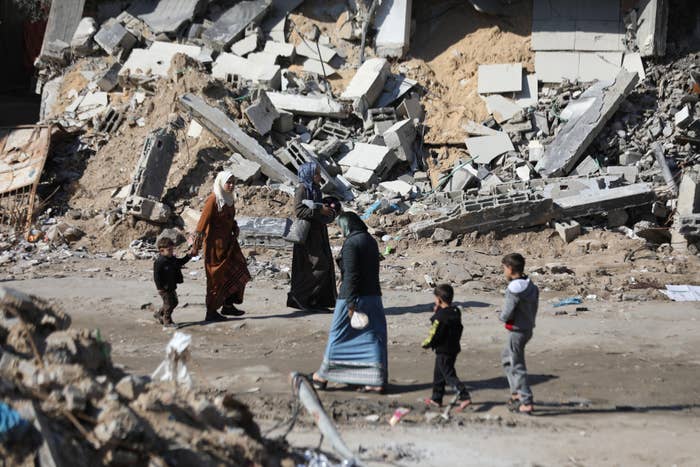 People walking by  buildings destroyed by bombs