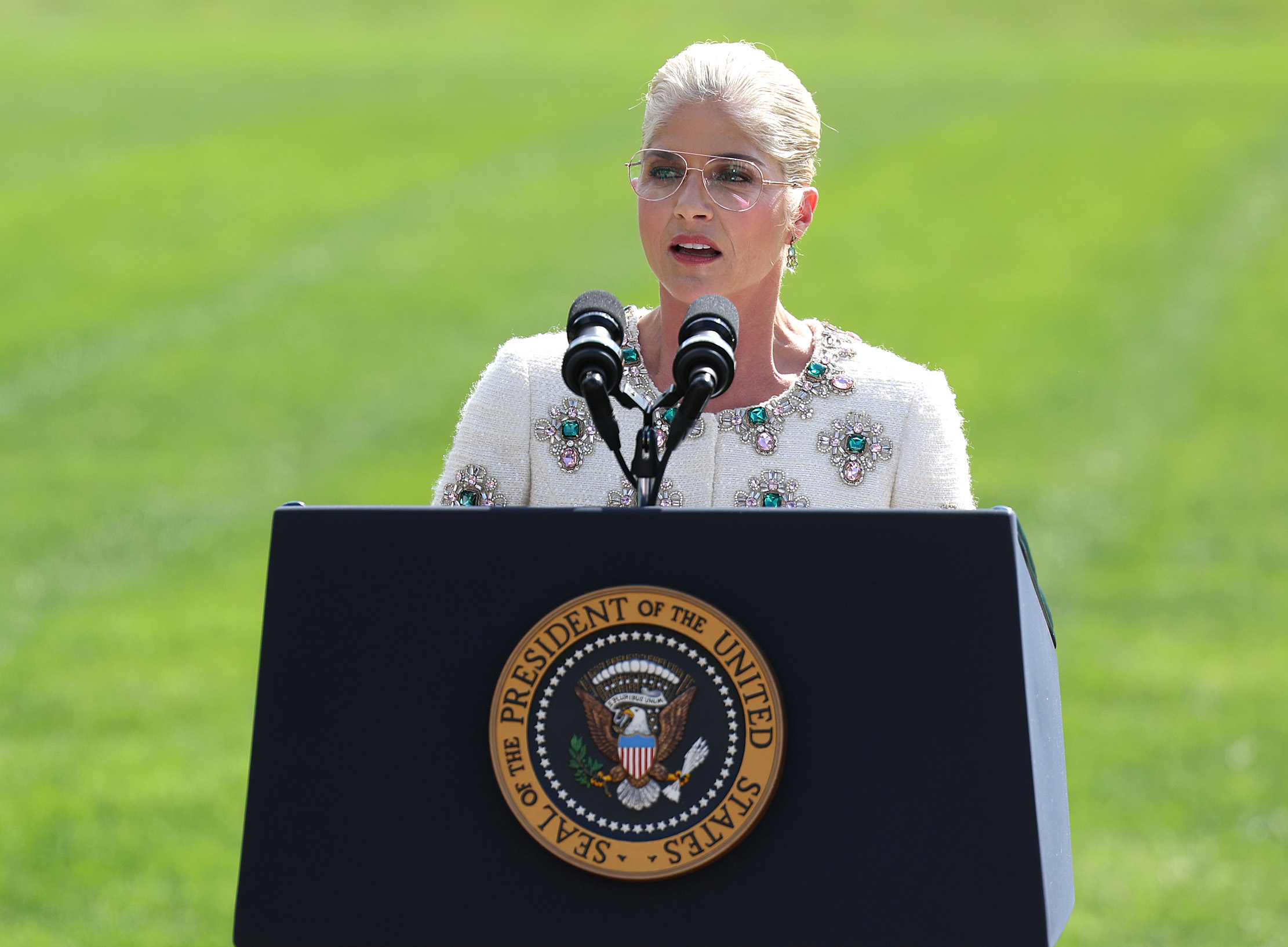 Selma in embellished outfit speaks at presidential podium outdoors