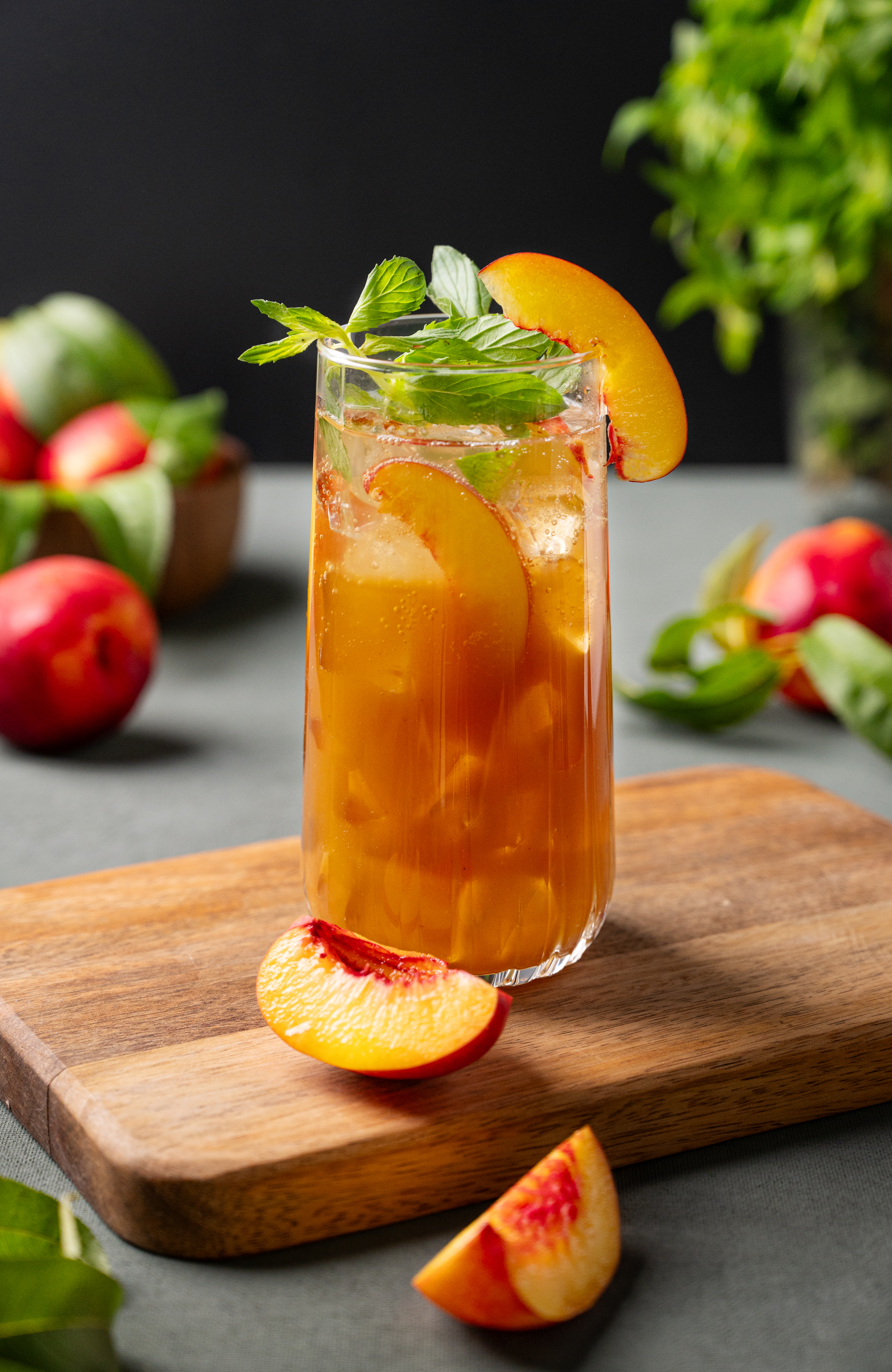 A glass of iced tea garnished with fresh mint and peach slices on a wooden board
