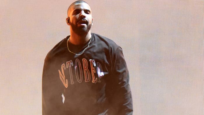 Drake on stage in a sweatshirt with the word &quot;October&#x27;s&quot; printed on it, performing with a mic