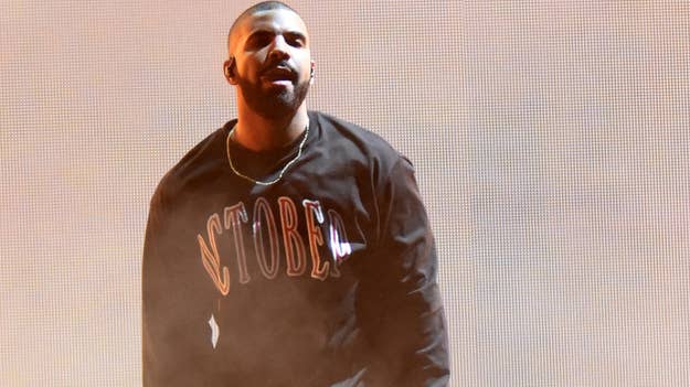 Drake on stage in a sweatshirt with the word "October's" printed on it, performing with a mic