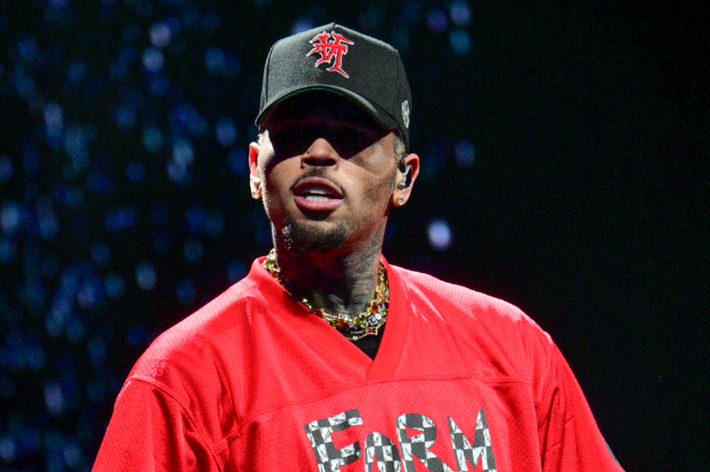 Chris Brown on stage wearing a cap and a red top with a logo