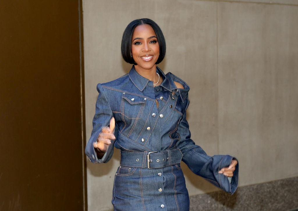 Kelly in a denim jacket and skirt set with silver buttons, smiling and waving