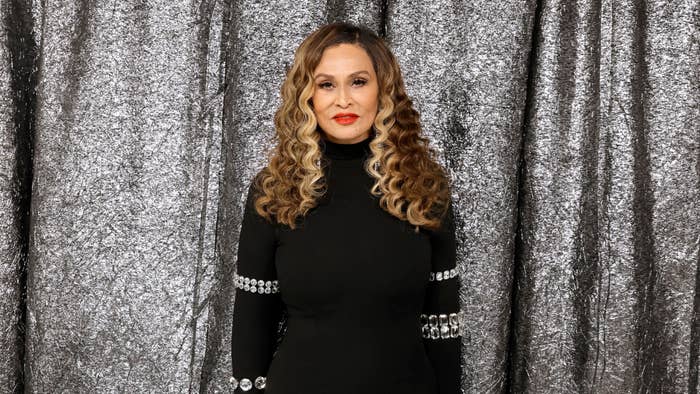 Ms. Tina Knowles in black dress with silver embellishments on sleeves poses in front of a shimmering backdrop