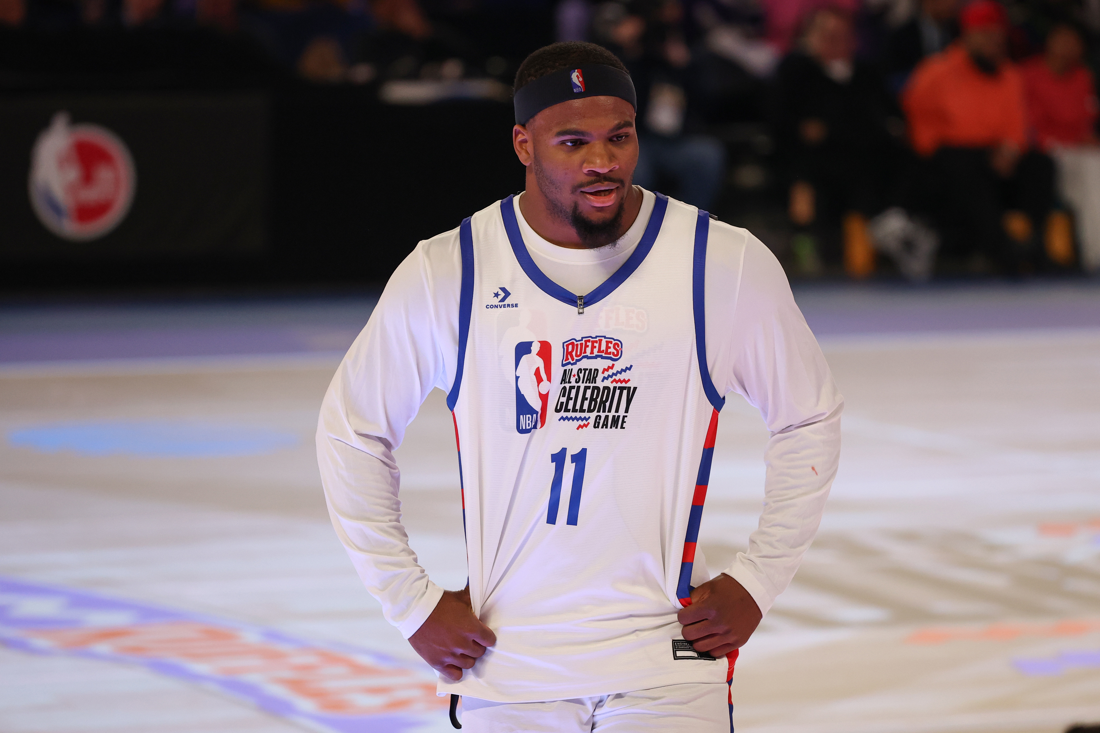 Person in a basketball jersey with &quot;Ruffles Celebrity Game&quot; text stands on the court