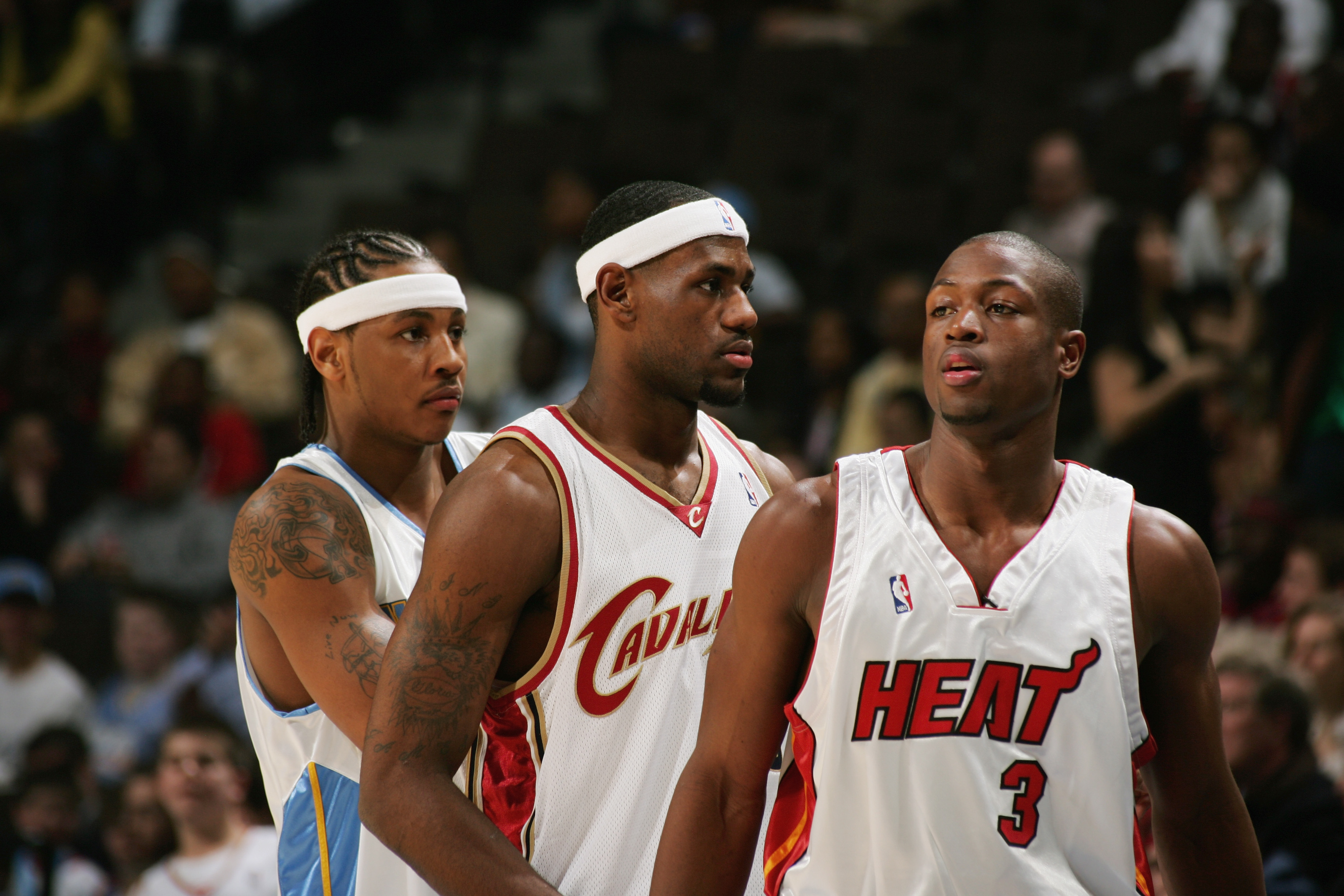 Three basketball players in jerseys, two from the Cavaliers and one from the Heat, focused during a game