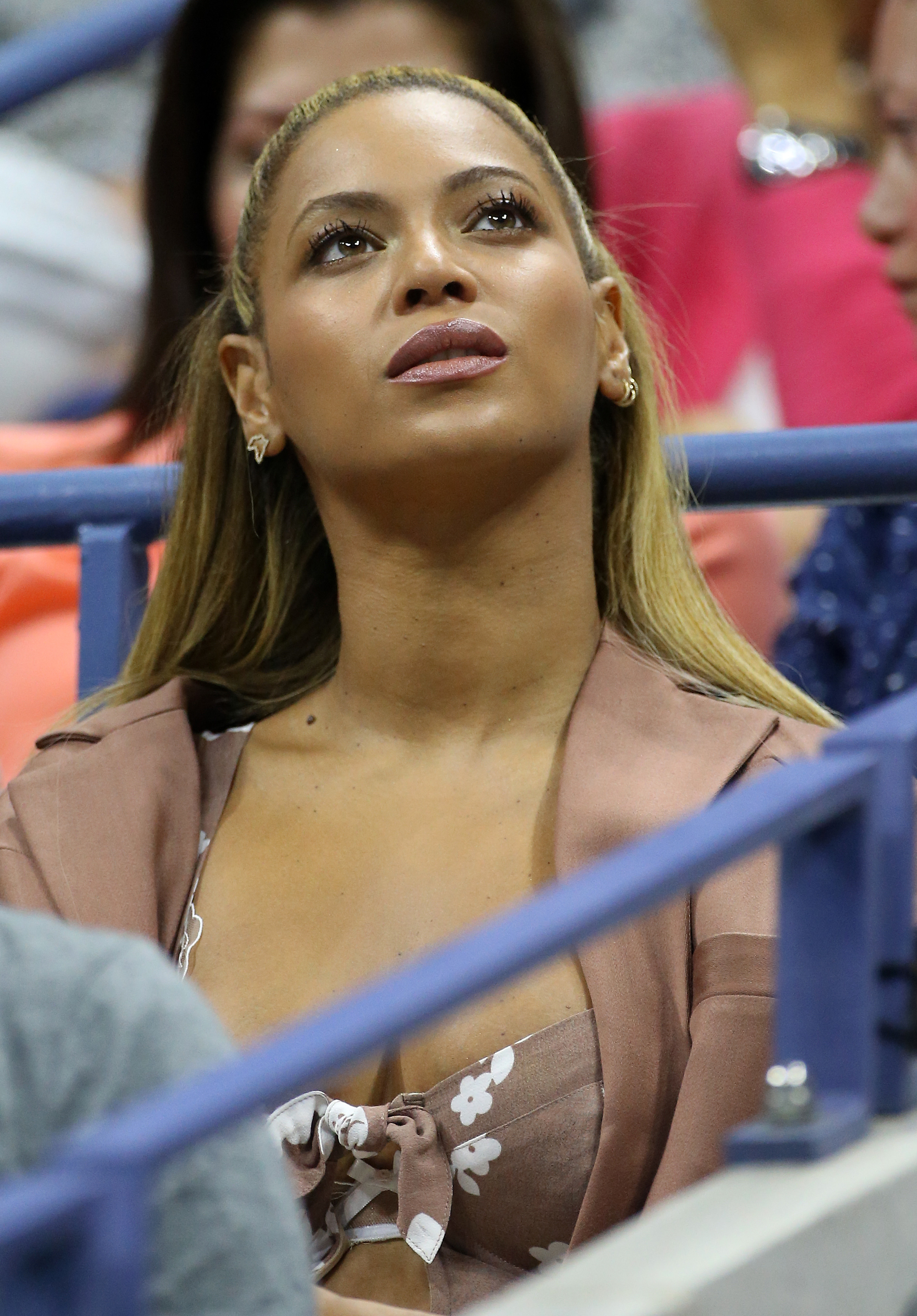 Beyoncé sitting, looking up, wearing a v-neck top with bow detail, at an indoor event