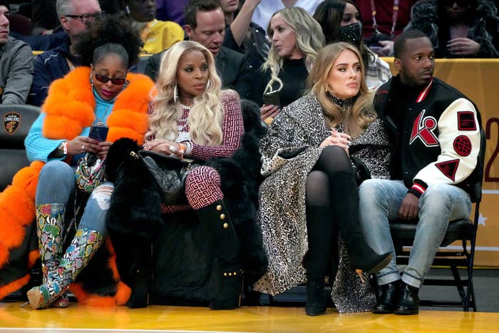 Mary J. Blige, Adele, and Rich Paul seated courtside at a basketball game, focused on the action