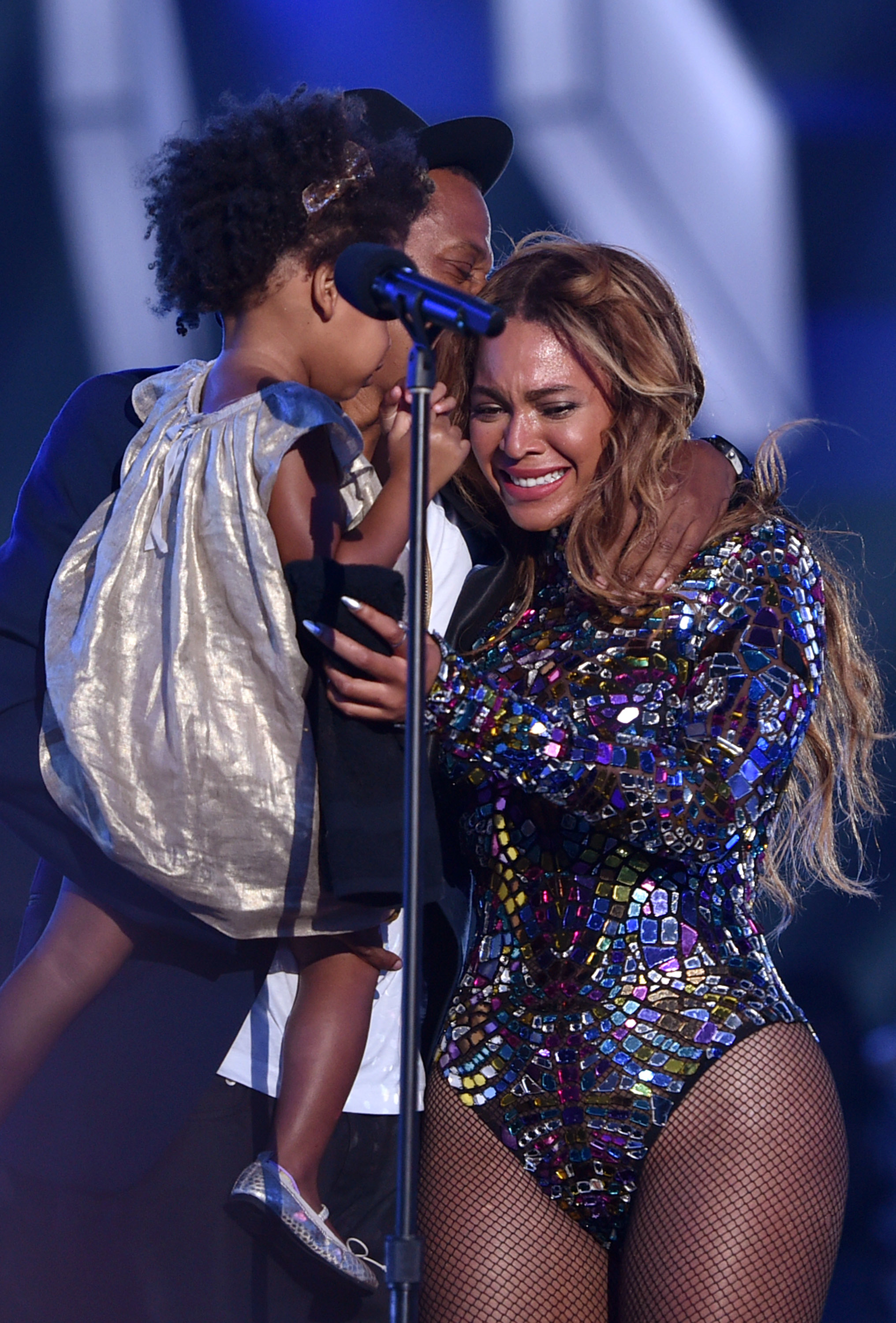 Jay-Z holding Blue Ivy, who is kissing Beyoncé on stage; Beyoncé in a sparkling bodysuit