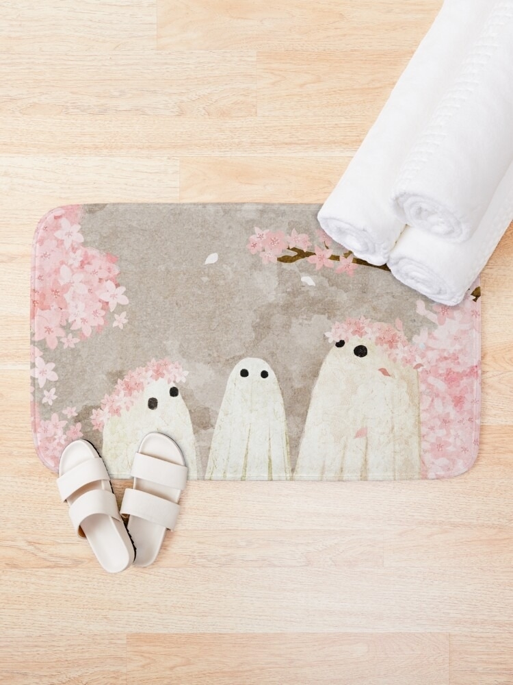 Patterned bath mat with cartoon ghosts, beside rolled towels and slippers. Used for cozy bathroom decor ideas