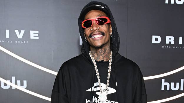 Wiz Khalifa smiles wearing sunglasses, chains, and a graphic tee at an event
