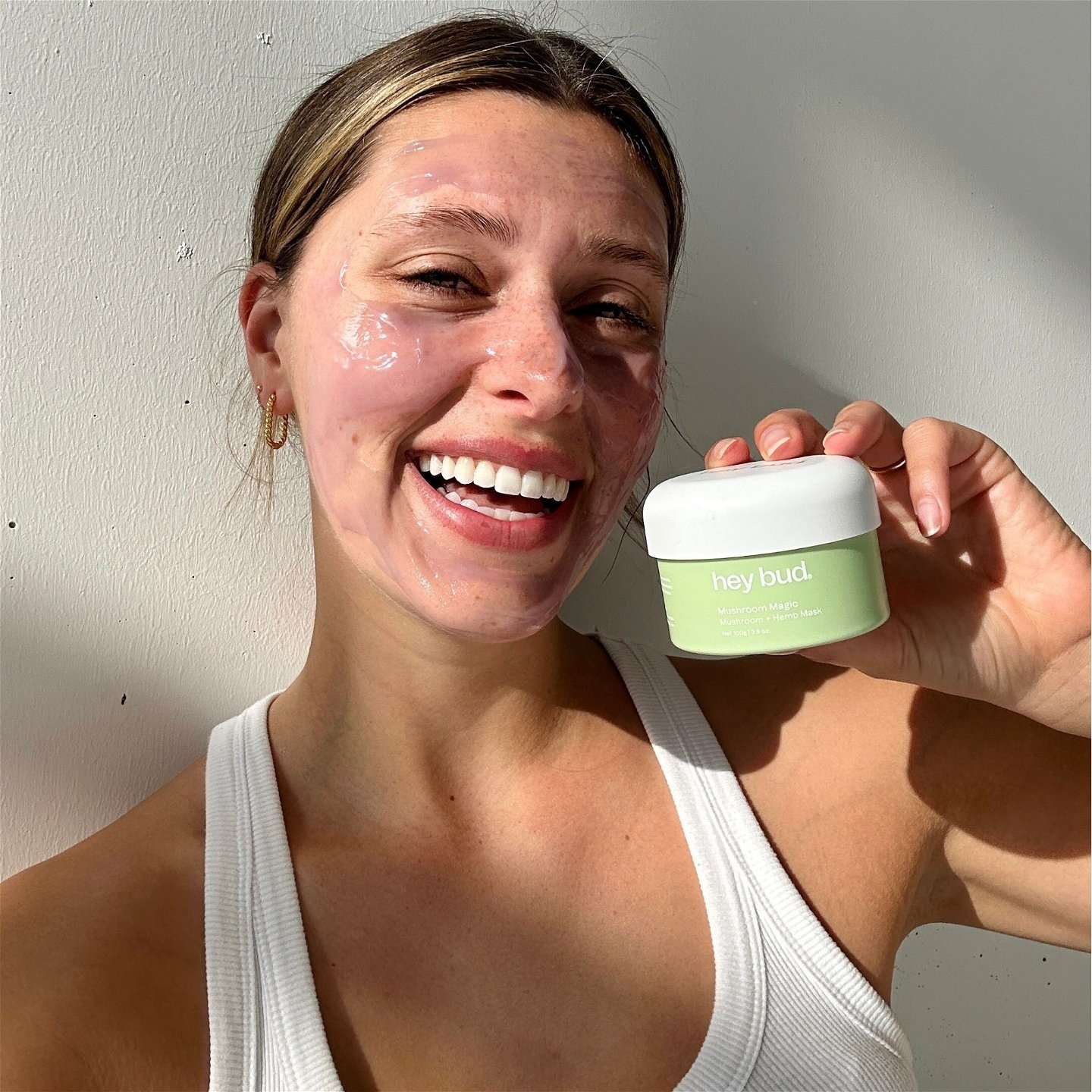 Woman with a skincare mask holding a Hey Bud skincare product
