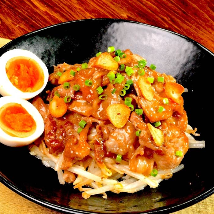 黒い皿に盛られたタレがかかった豚肉ともやしの料理、横には半分に切られたゆで卵。