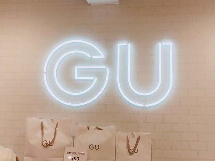 Neon sign &quot;GU&quot; on a wall above branded shopping bags