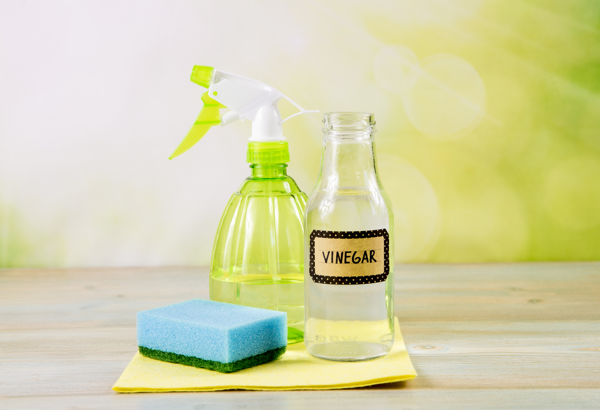 A bottle of vinegar next to a sponge and towel for cleaning