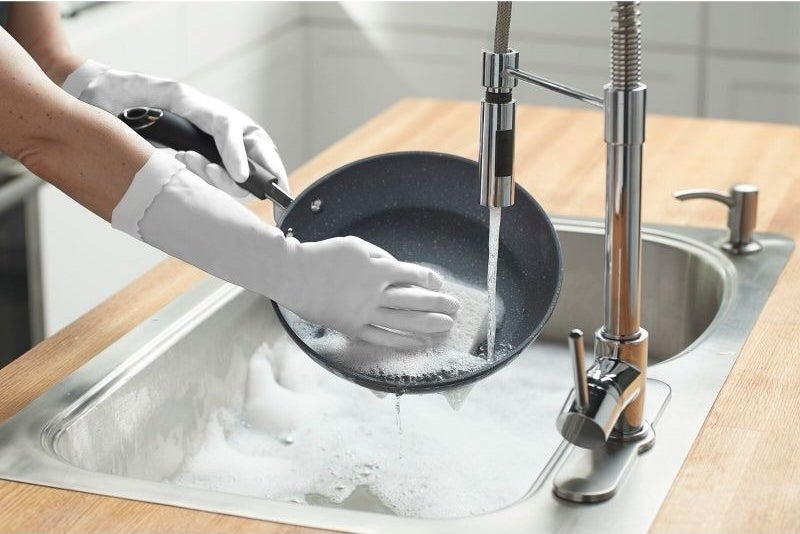 Hand wearing gloves clean a pan