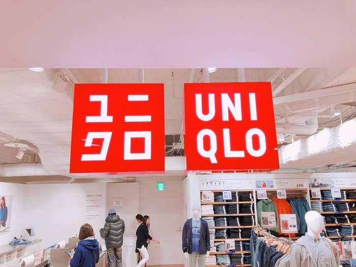 Signboards with &quot;UNIQLO&quot; text above clothing store displays, customers and mannequins visible
