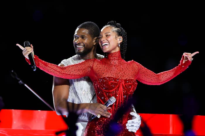 Usher holding Alicia Keys performers share a joyful moment onstage, one in a sparkling outfit, the other in a shimmering top