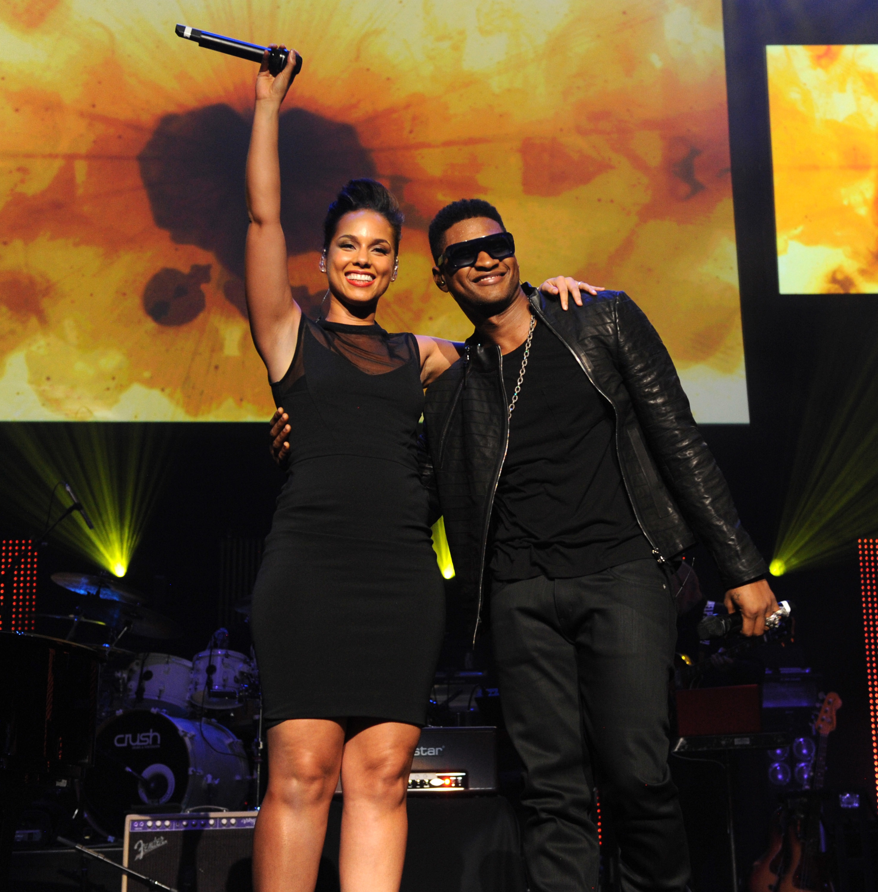 The two performers on stage, Alicia in a sleeveless dress and Usher in leather jacket and sunglasses, both smiling